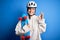 Young beautiful redhead skateboarder woman wearing safety helmet holding skate doing ok sign with fingers, excellent symbol