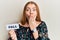 Young beautiful redhead woman holding fall word on paper covering mouth with hand, shocked and afraid for mistake