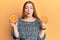 Young beautiful redhead woman holding fresh orange slices making fish face with mouth and squinting eyes, crazy and comical