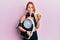 Young beautiful redhead woman holding weight machine to balance weight loss making fish face with mouth and squinting eyes, crazy