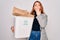 Young beautiful redhead woman recycling holding trash can with cardboard to recycle cover mouth with hand shocked with shame for