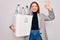 Young beautiful redhead woman recycling holding trash can with plastic bottles to recycle doing ok sign with fingers, excellent