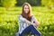 Young beautiful redhead woman sits on a green meadow, looking at camera