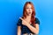 Young beautiful redhead woman wearing casual clothes over blue background surprised pointing with finger to the side, open mouth