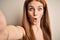 Young beautiful redhead woman wearing diadem make selfie by the camera scared in shock with a surprise face, afraid and excited