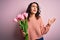 Young beautiful romantic woman with curly hair holding bouquet of pink tulips crazy and mad shouting and yelling with aggressive