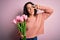 Young beautiful romantic woman with curly hair holding bouquet of pink tulips Doing peace symbol with fingers over face, smiling