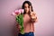 Young beautiful romantic woman with curly hair holding bouquet of pink tulips Pointing with finger up and angry expression,