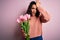 Young beautiful romantic woman with curly hair holding bouquet of pink tulips surprised with hand on head for mistake, remember