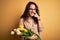 Young beautiful romantic woman with curly hair holding bouquet of yellow tulips Pointing with hand finger to face and nose,