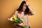 Young beautiful romantic woman with curly hair holding bouquet of yellow tulips surprised with hand on head for mistake, remember