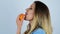 Young beautiful sexy blonde woman licks half of fresh orange smiling on isolated white background