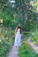 Young beautiful Slavic girl with long hair and Slavic ethnic attire walking along the trail in the summer forest