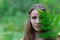 A young beautiful Slavic girl with long hair and Slavic ethnic dress covered her face with a fern leaf