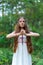 A young beautiful Slavic girl with long hair and Slavic ethnic dress stands in a summer forest with a ritual dagger in her hands