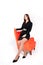A young, beautiful, slender girl in a black dress and black shoes stands next to a red armchair on a white background. Isolated. A