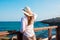 Young beautiful slender woman in sunhat with long hair in boho style clothes at the shore looking and the sea clear blue sky