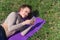 Young with a beautiful smile girl sits on the grass and looks into the phone. Sports lady laughs at phone