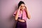 Young beautiful sportswoman with curly hair doing sport using towel over pink background with hand on head for pain in head