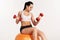 Young beautiful sportswoman with dumbbells exercising on fitball