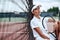 Young beautiful sportswoman with tennis racket sitting at tennis net on tennis court. Sports Fashion