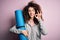 Young beautiful sporty woman with curly hair and piercing holding mat doing yoga doing ok sign with fingers, excellent symbol