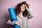 Young beautiful sporty woman with curly hair and piercing holding mat doing yoga stressed with hand on head, shocked with shame