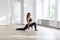 Young beautiful sporty woman wearing black sportswear practicing sport exercises, doing lunges near window in gym, stretching legs