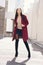 Young beautiful stylish woman walking in burgundy coat, street style, spring summer trend, dark skirt, beige jacket, flirty
