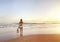 Young beautiful surfer girl walking towards surf at sunrise