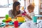 Young beautiful teacher and toddler playing with plastic food and cuttlery toys at kindergarten