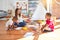 Young beautiful teacher and toddlers sitting on the floor drawing around lots of toys at kindergarten