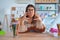 Young beautiful teacher woman wearing sweater and glasses sitting on desk at kindergarten Shouting frustrated with rage, hands