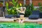 Young beautiful teenage girl sitting near exotic swimming pool with coconut and posing in water