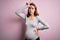 Young beautiful teenager girl pregnant expecting baby over isolated pink background making fun of people with fingers on forehead