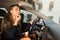 Young beautiful woman applying lipstick while sitting in car behind the weel using a sun visor mirror