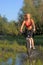 Young beautiful woman with bicycle going through water by the river