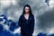 Young beautiful woman with black hair and in the dark blue cloak with hood at the sky background