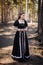 Young, beautiful woman in a black medieval dress walks through the gloomy pine forest.