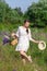 Young beautiful woman with bouquet of flowers in basket at sunny field. Pretty vintage girl in white dress and hat in