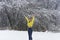 Young beautiful woman in bright yellow sweater rejoices  first snowfall, raising hands up. Lady in winter forest for walk,  first