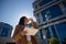 Young and beautiful woman in a brown coat and drinking coffee, checking social networks on her tablet as she leaves her office at