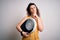 Young beautiful woman with curly hair holding weighing machine and tape measure serious face thinking about question, very