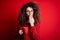 Young beautiful woman with curly hair and piercing drinking red cup of coffee cover mouth with hand shocked with shame for