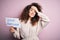 Young beautiful woman with curly hair and piercing holding paper with love yourself message stressed with hand on head, shocked
