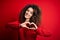 Young beautiful woman with curly hair and piercing wearing casual red sweater smiling in love doing heart symbol shape with hands