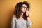 Young beautiful woman with curly hair and piercing wearing striped shirt and glasses mouth and lips shut as zip with fingers