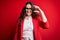 Young beautiful woman with curly hair wearing jacket and glasses over red background smiling and confident gesturing with hand