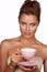 Young beautiful woman with dark hair picked up holding a ceramic cup and saucer pale pink drink tea or coffee on a white back