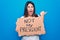 Young beautiful woman on disagreement holding banner with not my president message pointing thumb up to the side smiling happy